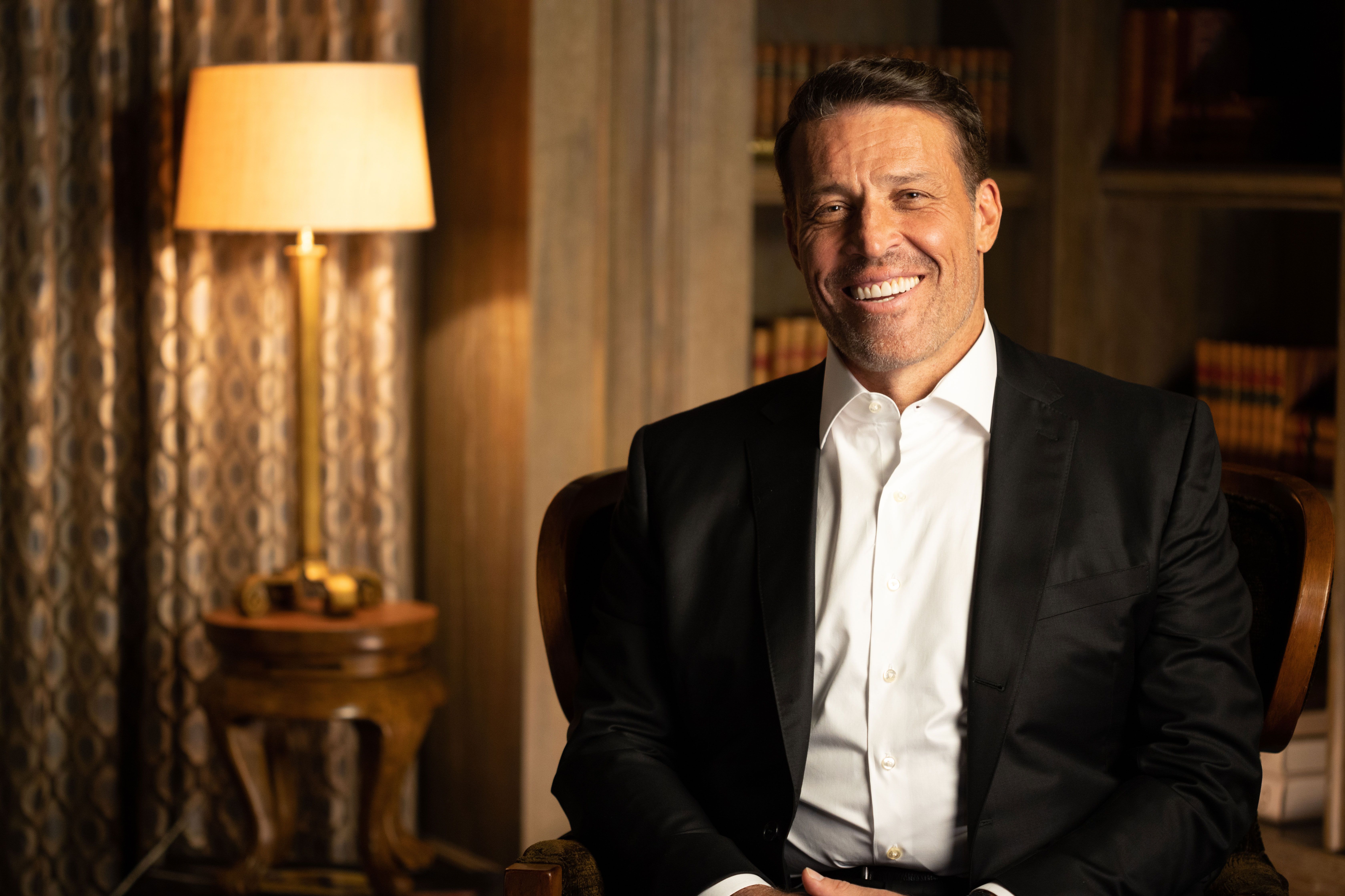 a man in a suit and white shirt is sitting in a chair and smiling .