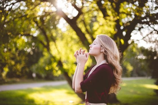a woman is praying in a park with her eyes closed .
