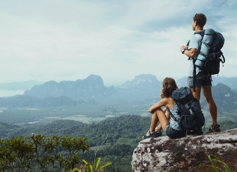 a man and a woman with backpacks looking out over a mountain range