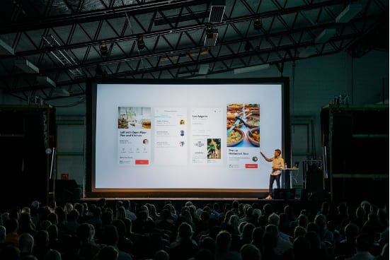a man is giving a presentation to a large group of people in front of a large screen .