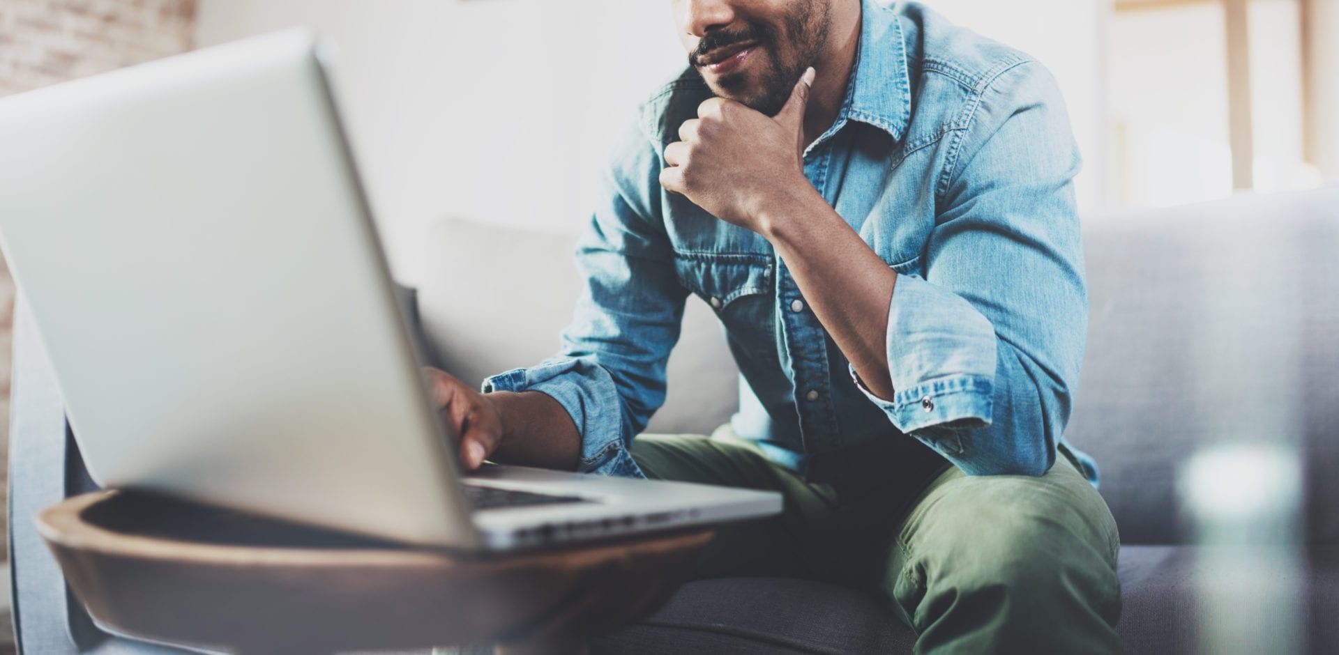a man is sitting on a couch using a laptop computer .