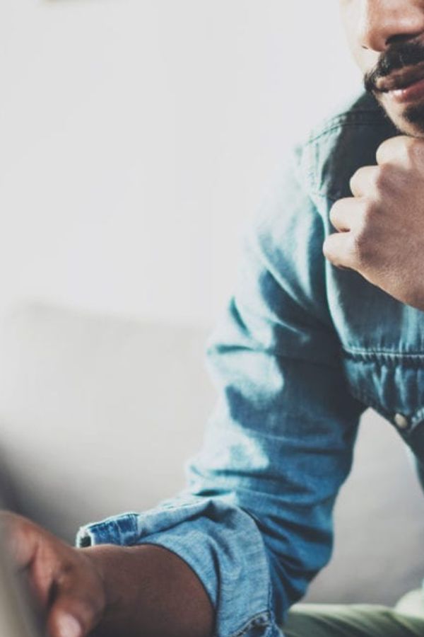a man is sitting on a couch using a laptop computer .