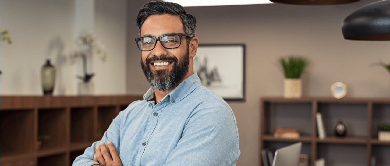 a man with glasses and a beard is smiling with his arms crossed
