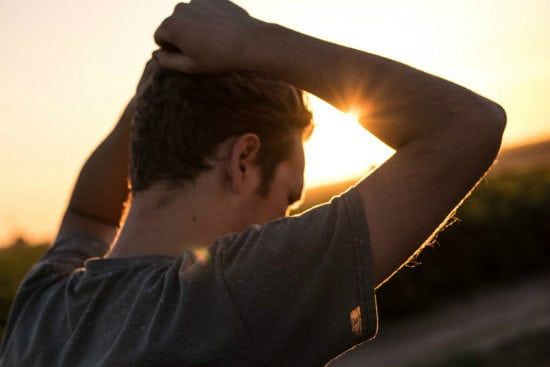 a man is holding his head in front of the sun at sunset .
