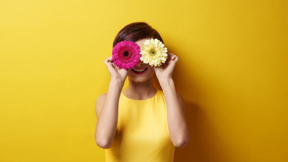 a woman in a yellow dress is holding two flowers in front of her eyes .