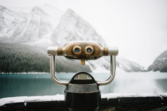 a binoculars is sitting on a ledge overlooking a lake with mountains in the background .