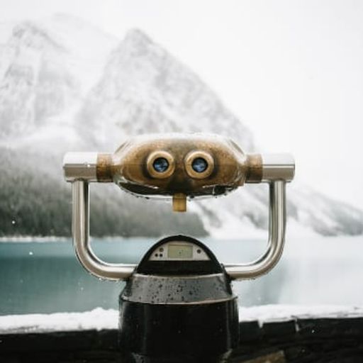 a binoculars is sitting on a ledge overlooking a lake with mountains in the background .