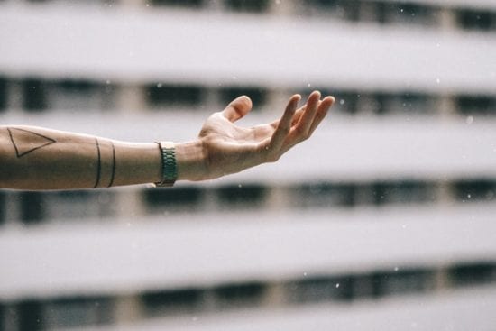 a person with a tattoo on their arm is reaching out towards the rain .