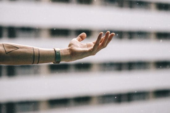 a person with a tattoo on their arm is reaching out towards the rain .