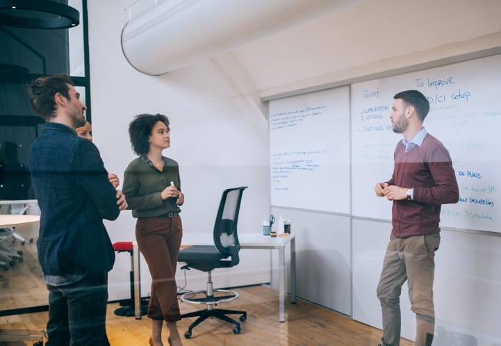 a group of people are standing in front of a whiteboard in an office .