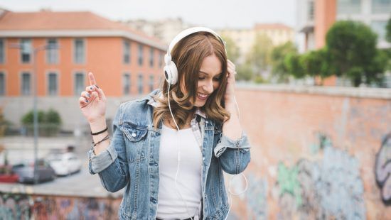 a woman wearing headphones and a denim jacket is dancing while listening to music .