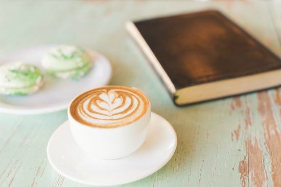 a cup of cappuccino on a saucer next to a book on a table .