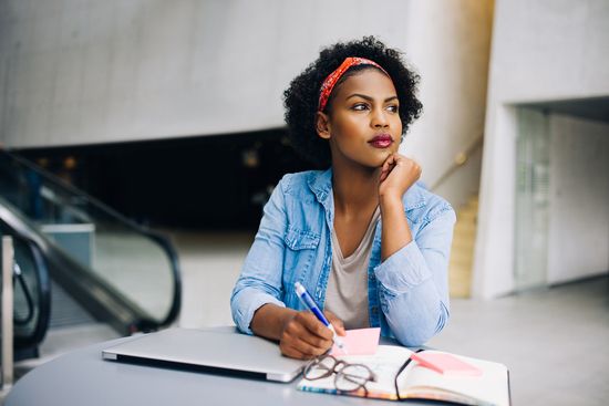 a woman is sitting at a table with a laptop and a notebook .