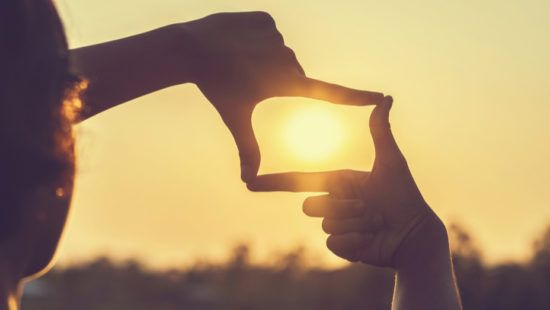 a person is making a frame around the sun with their hands .
