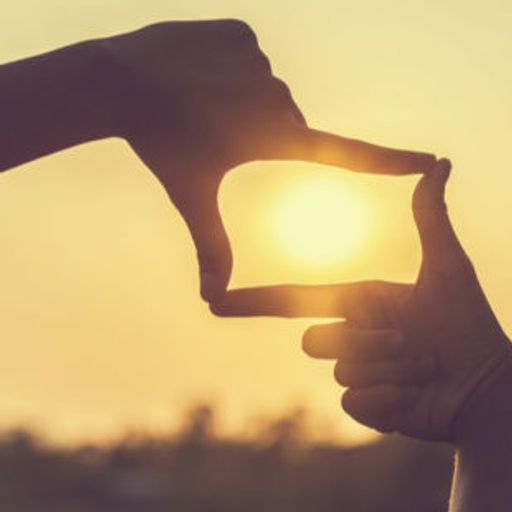 a person is making a frame around the sun with their hands .