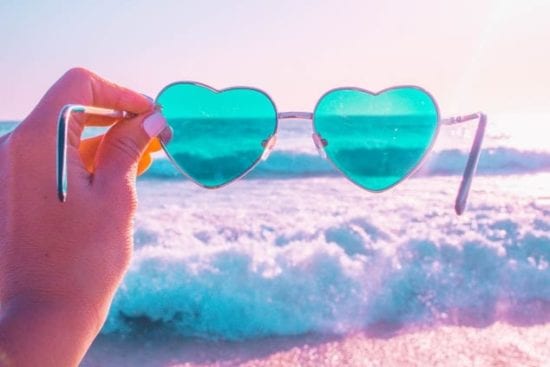 a person is holding a pair of heart shaped sunglasses on the beach .