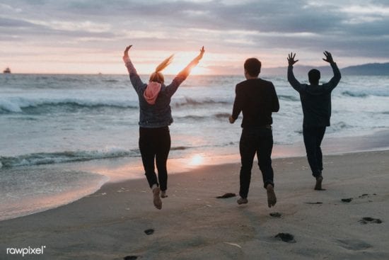 three people are jumping in the air on the beach at sunset .