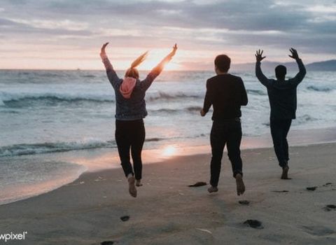 three people are jumping in the air on the beach at sunset .