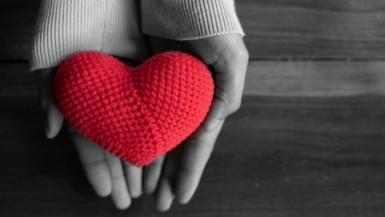 a person is holding a red crocheted heart in their hands .