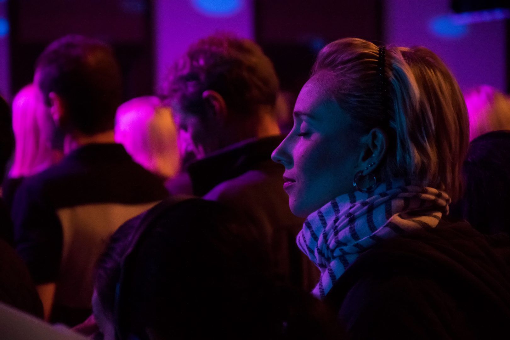 a woman is sitting in a crowd of people at a concert with her eyes closed .