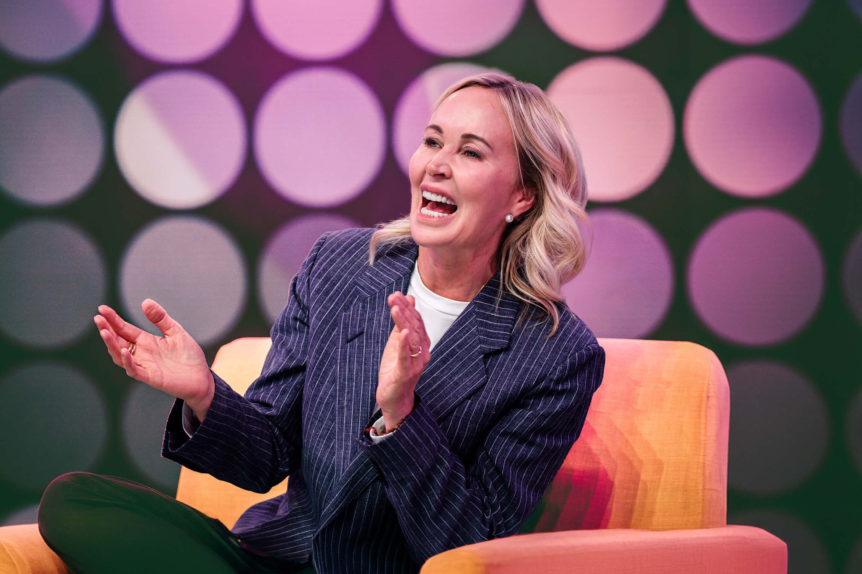 a woman is sitting in a chair with her hands folded and smiling .