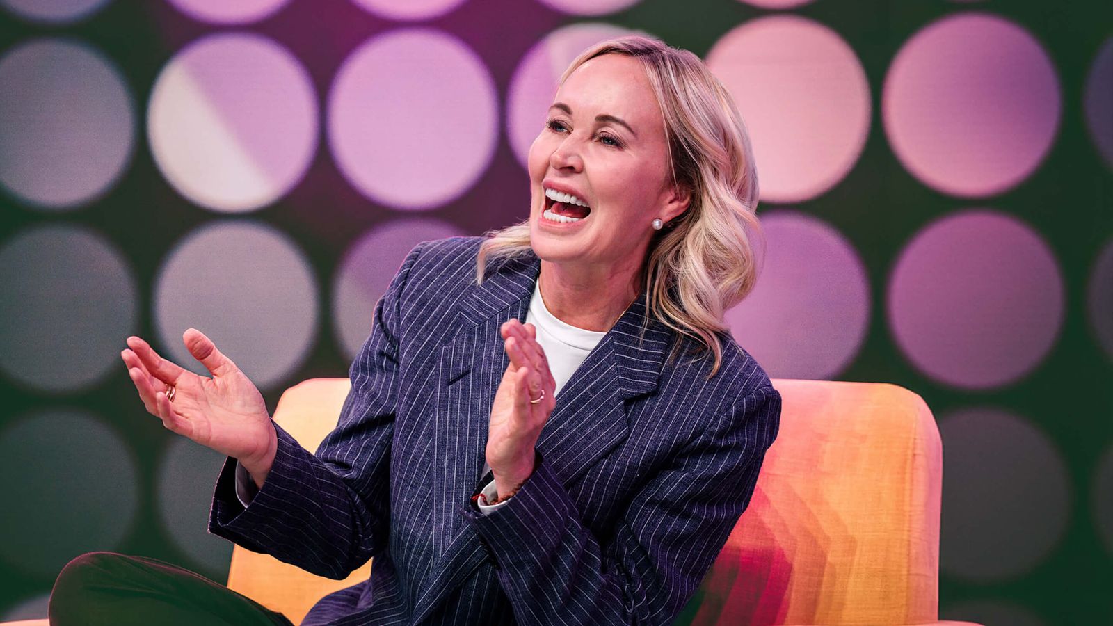a woman is sitting in a chair with her hands folded and smiling .