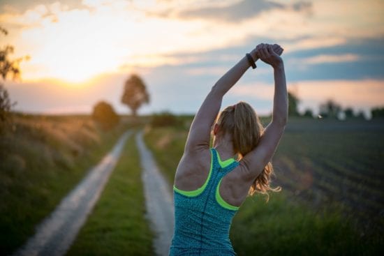 a woman is stretching her arms on a dirt road at sunset .