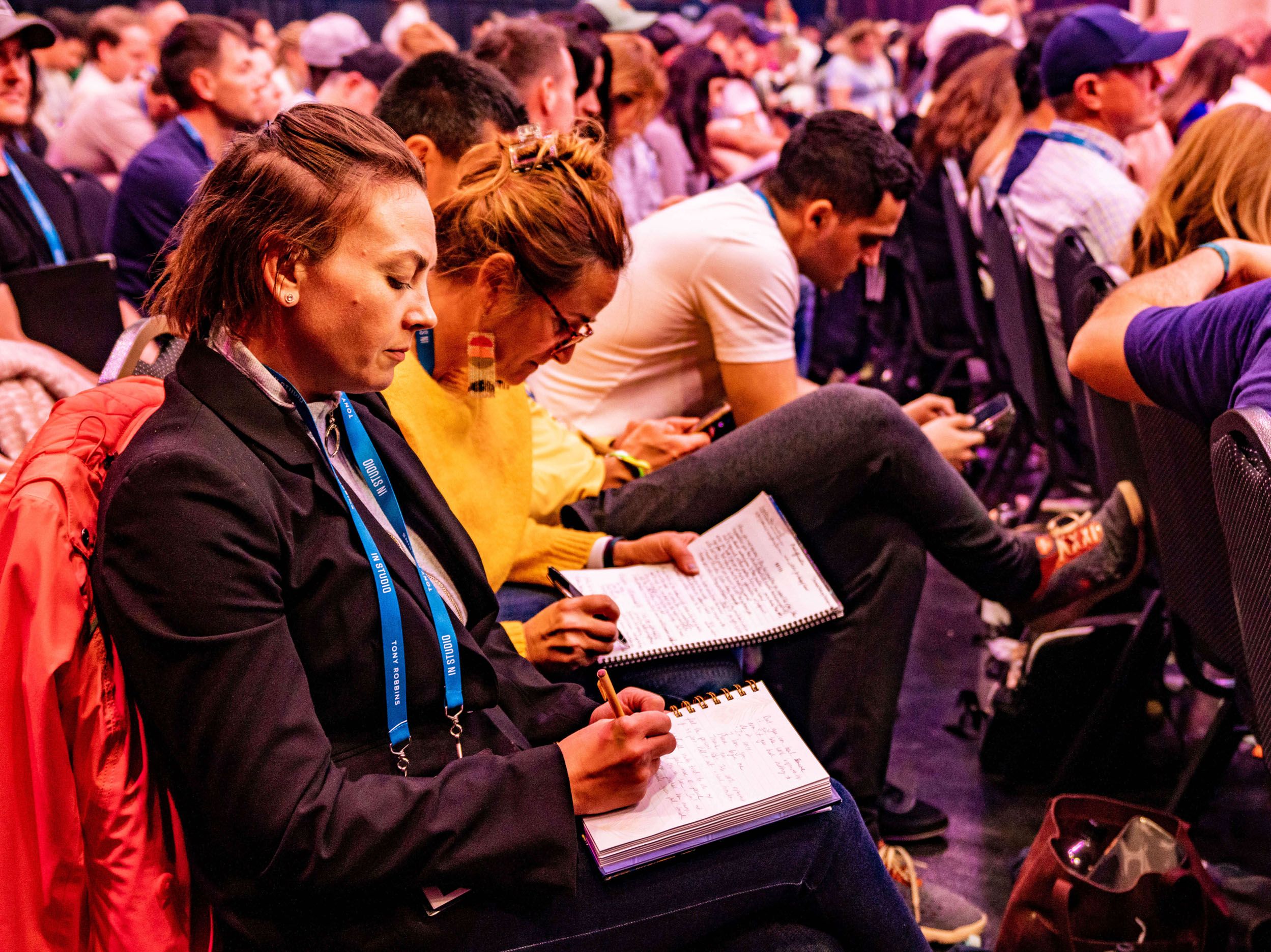 a group of people are sitting in a stadium taking notes in notebooks .