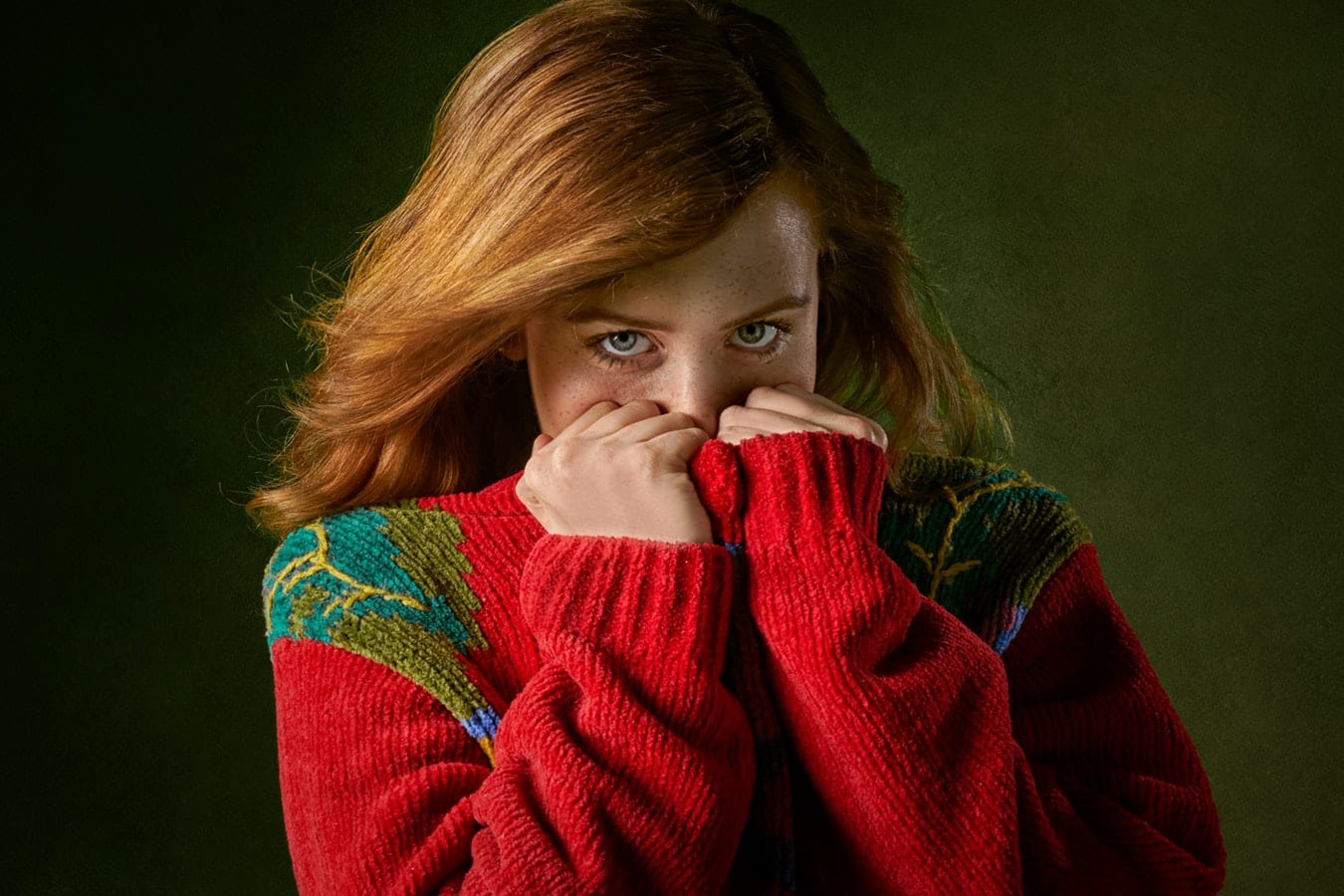 a woman in a red sweater is covering her face with her hands .