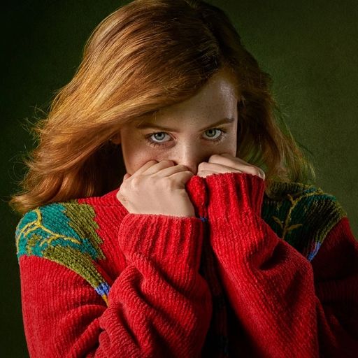 a woman in a red sweater is covering her face with her hands .