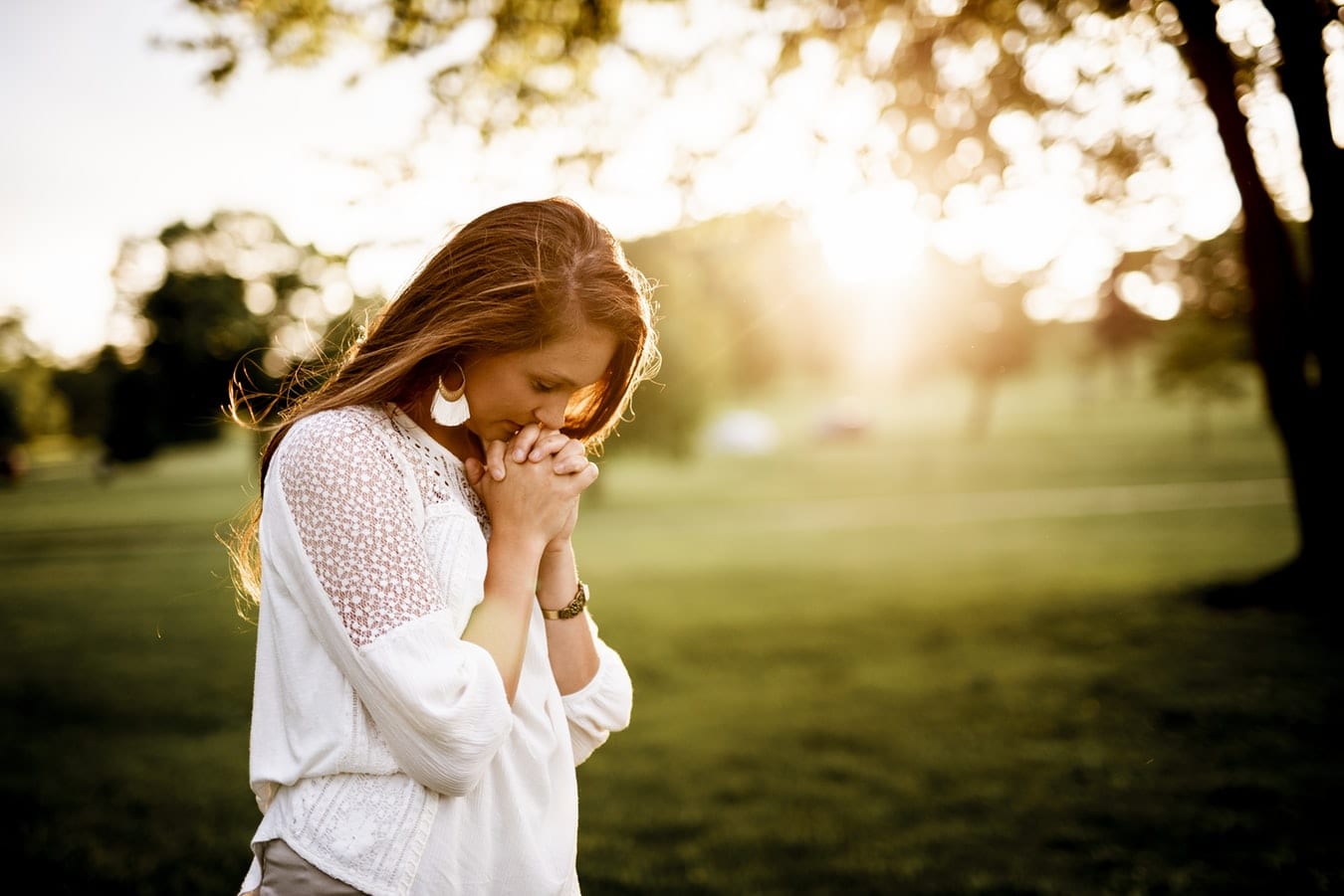 a woman is praying in a park with her hands folded .