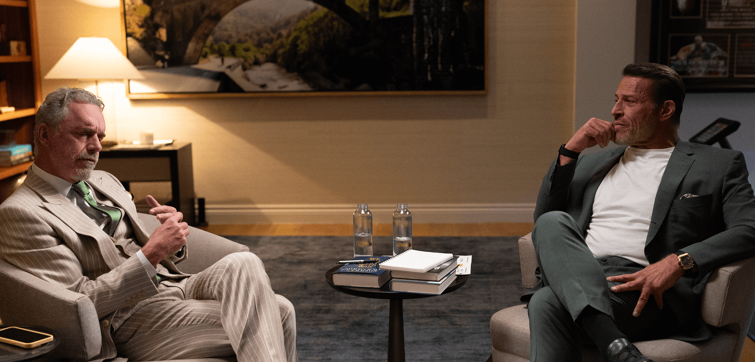 a man in a suit sits next to another man in a chair