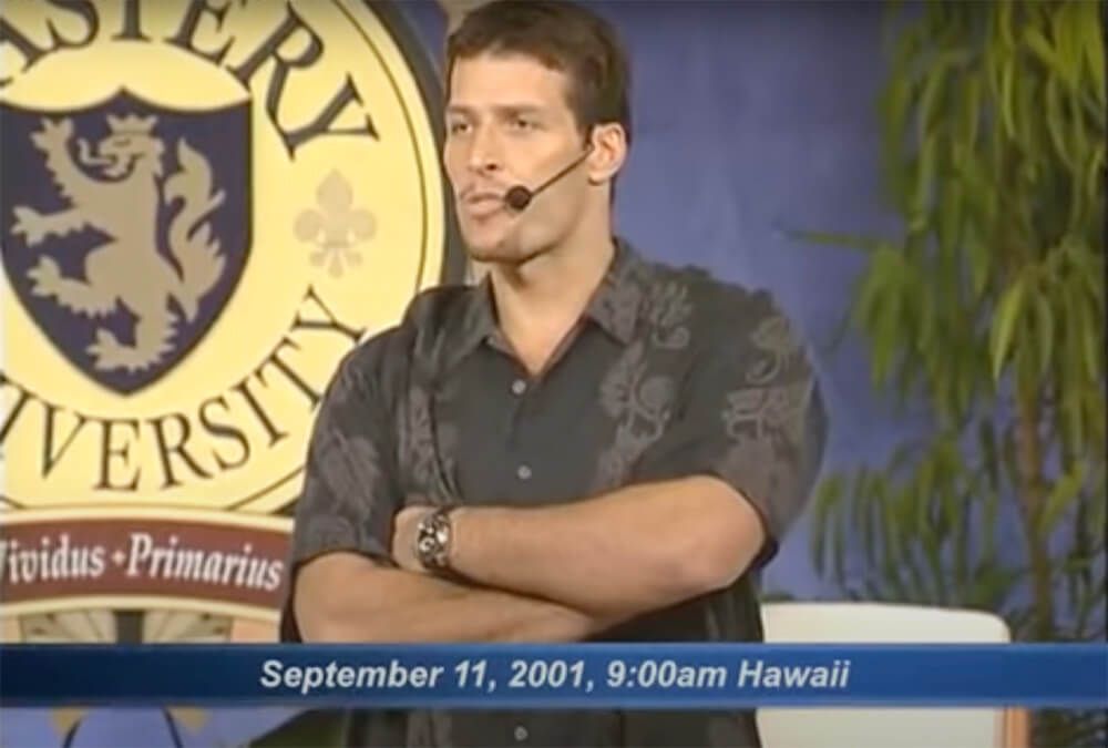 a man wearing a microphone is standing in front of a university logo .
