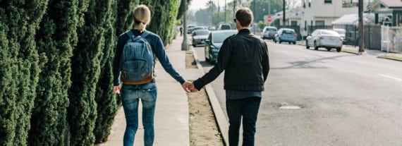 a man and a woman are walking down a sidewalk holding hands .