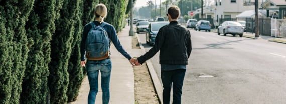 a man and a woman are walking down a sidewalk holding hands .
