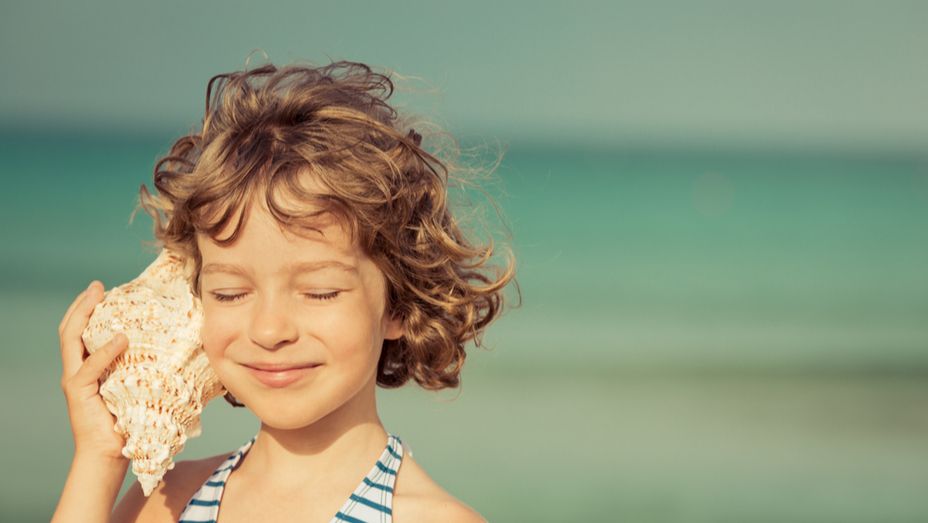 a little girl is listening to a sea shell on the beach .