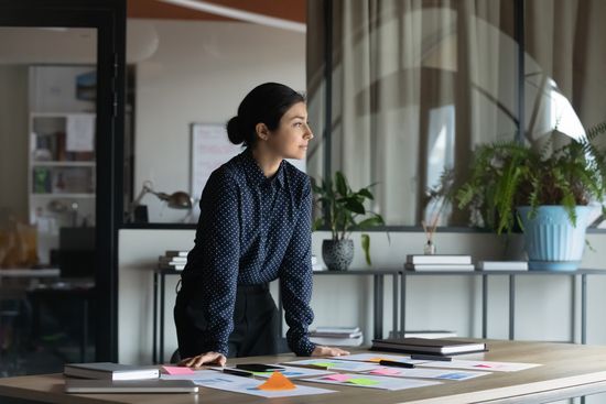 a woman is leaning on a table in an office looking out the window .