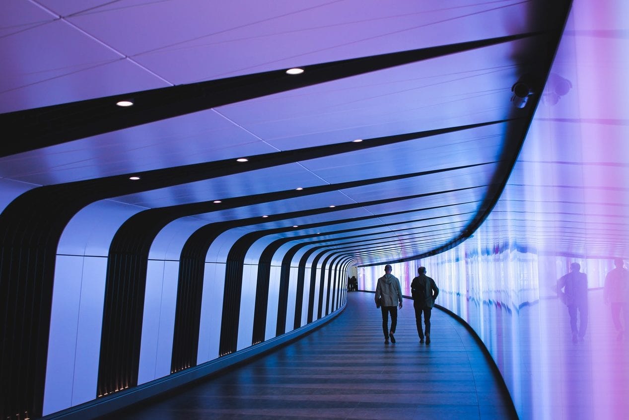 two men are walking through a purple and blue tunnel .
