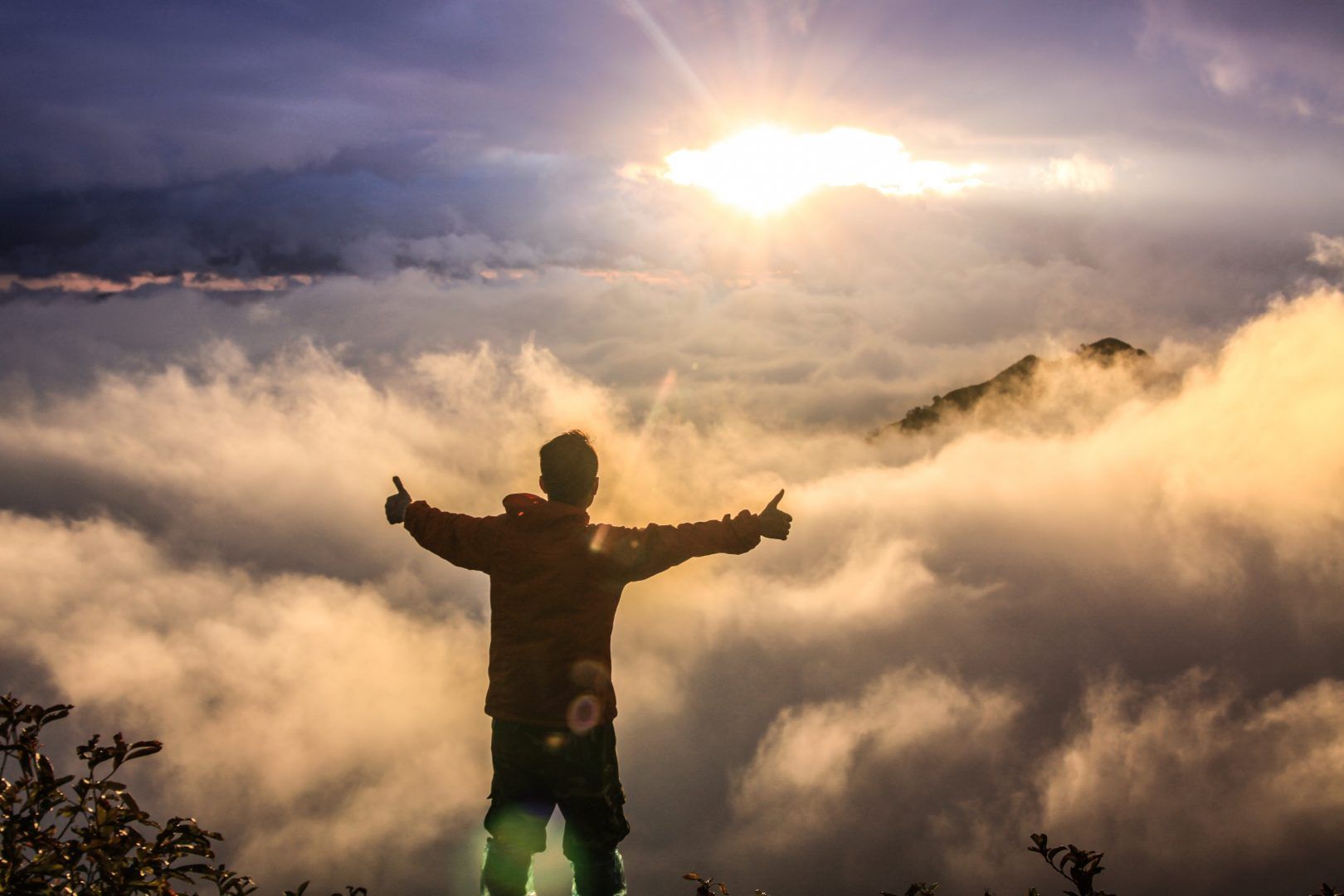 a man is standing on top of a mountain with his arms outstretched .