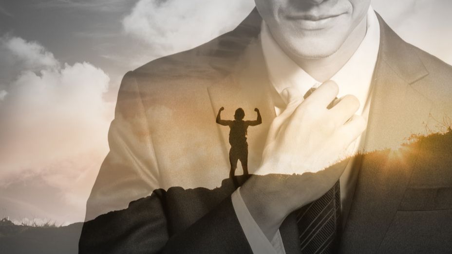 a man in a suit and tie is standing on top of a mountain with his arms outstretched .
