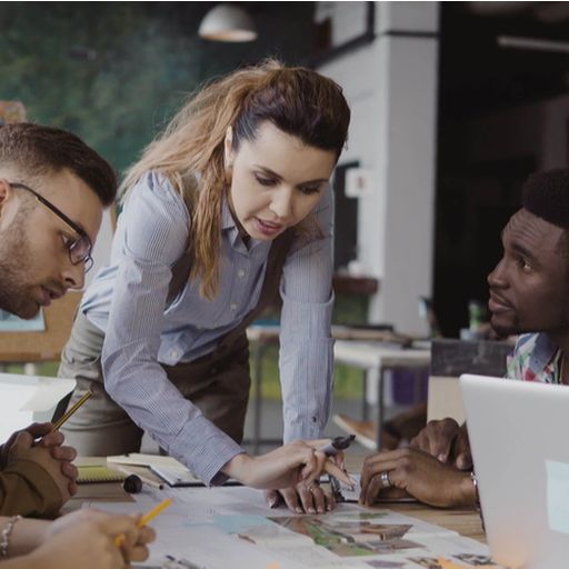 a group of people are sitting around a table looking at a laptop .