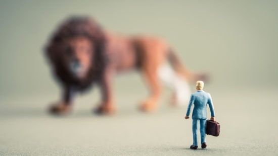 a miniature man with a briefcase is standing in front of a toy lion .