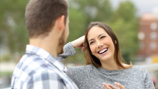 a woman is smiling while talking to a man in a park .