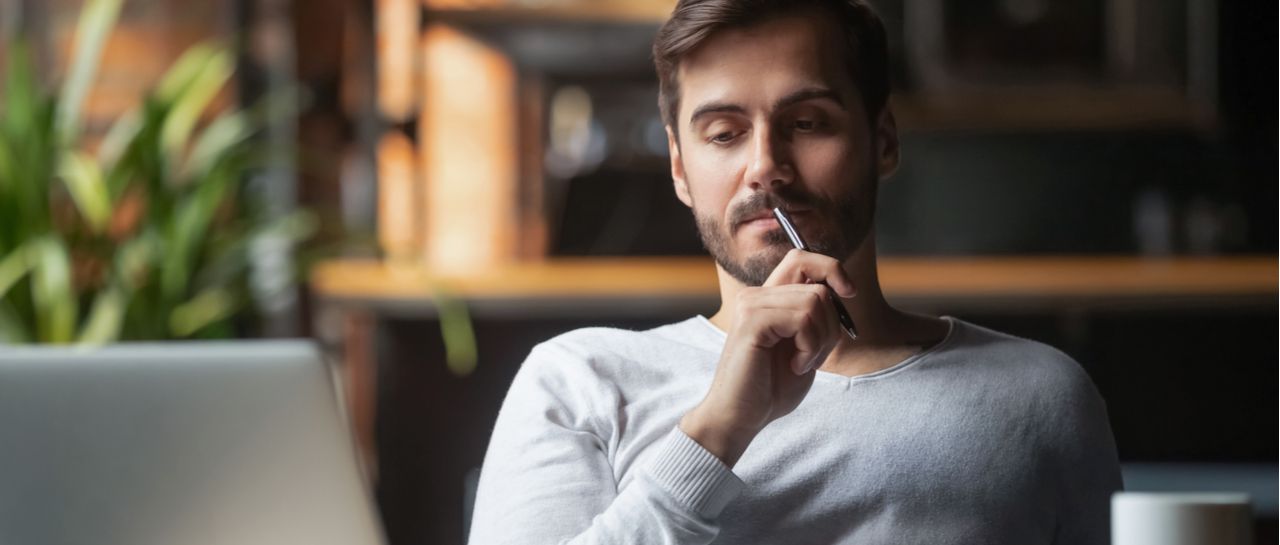 a man is sitting in front of a laptop computer with a pen in his mouth .