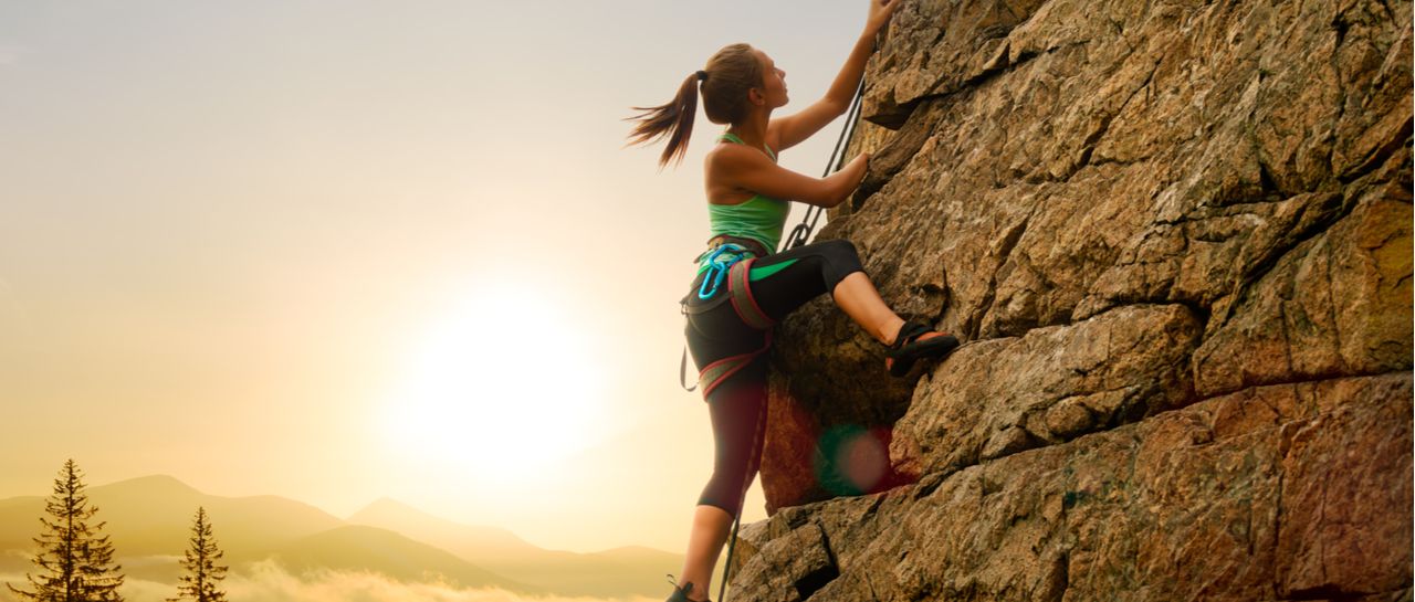a woman is climbing up a rock wall at sunset .