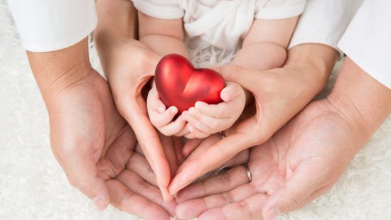 a family is holding a red heart in their hands