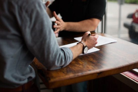 two men are sitting at a table having a conversation .
