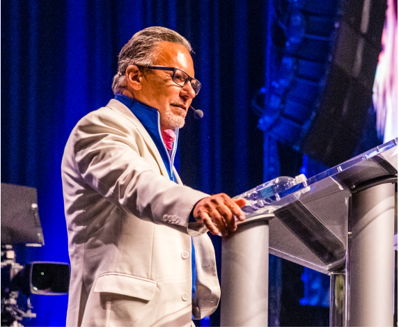 a man in a white suit stands at a podium with a microphone