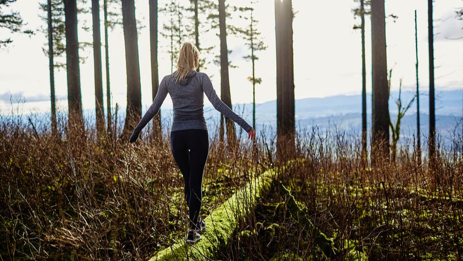 a woman is walking across a log in the woods .