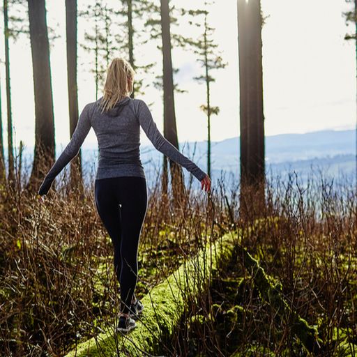 a woman is walking across a log in the woods .